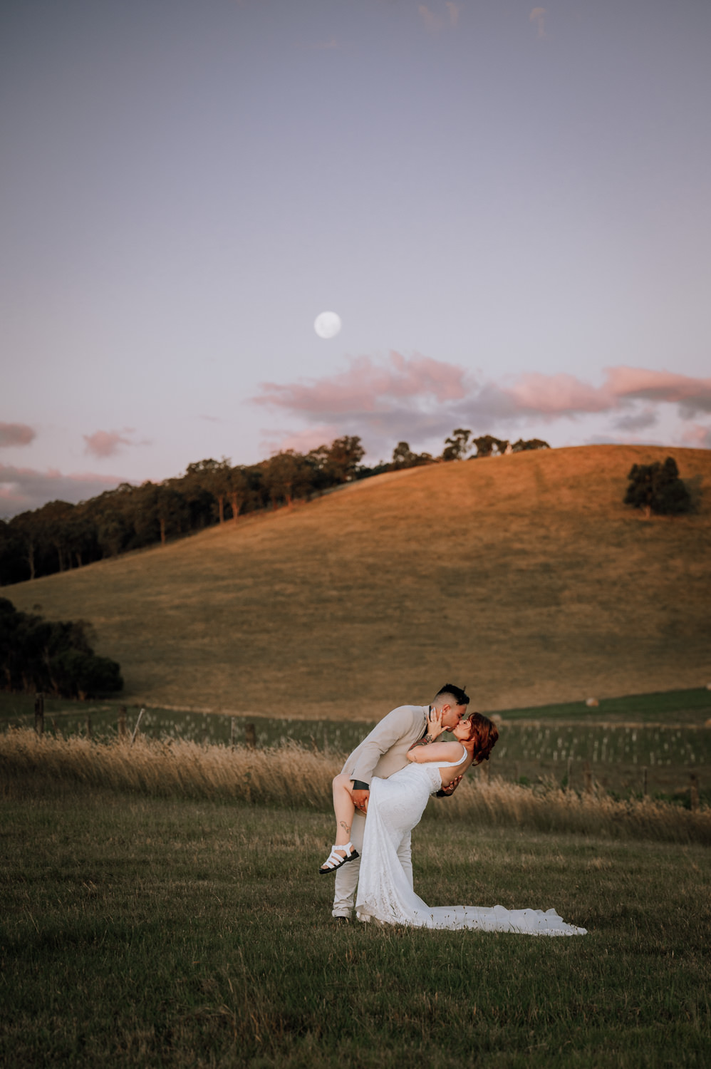 Yarra Valley wedding couple in a dip kiss at sunset while the moon rises over the hill behind them